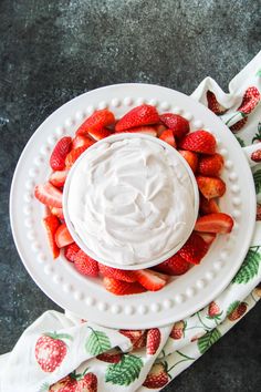 a white plate topped with strawberries on top of a cloth next to a bowl of whipped cream