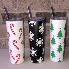 three christmas themed tumblers are lined up against a brick wall