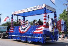 a parade float with people riding in it and flags on the back, along with an american flag banner