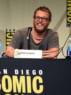 a man sitting at a table with a microphone in front of him and two bottled water bottles behind him