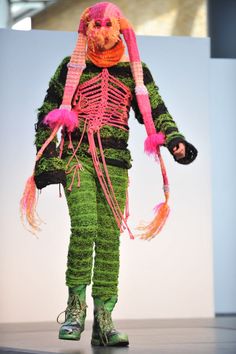 a woman in green and pink costume walking down the runway with her hand on her hip