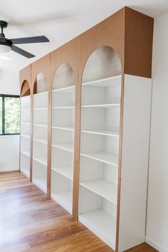 a room with white shelving and wooden flooring in front of a ceiling fan