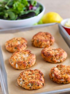 several crab cakes on a baking sheet next to a bowl of salad