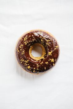 a chocolate donut with gold sprinkles on it sitting on a white surface