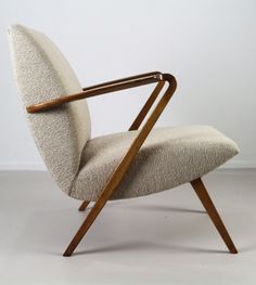 an upholstered chair with a wooden armrest and curved seat, in front of a white wall