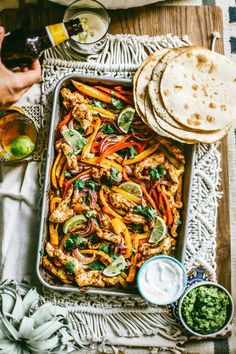 a tray filled with chicken and veggies next to pita bread