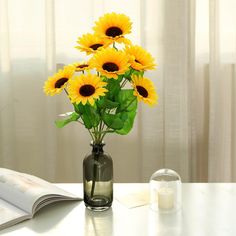 a vase filled with yellow sunflowers sitting on top of a table next to an open book