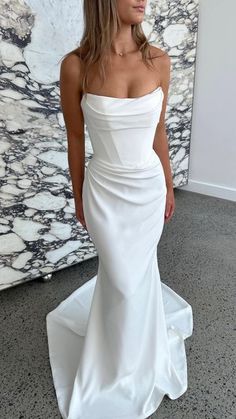 a woman wearing a white dress standing in front of a marble wall