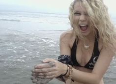 a woman in a bathing suit holding something up to her face while standing in the water