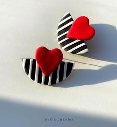 two heart shaped pins sitting on top of a white surface with black and white stripes