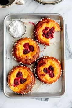 four pastries with raspberries on top and powdered sugar in the middle