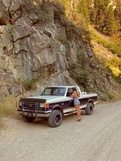 a woman standing in the bed of a pick up truck next to a large rock