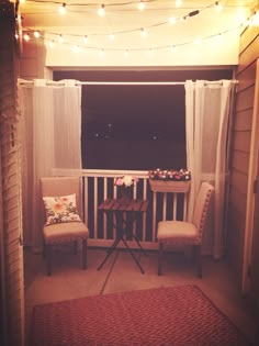 two chairs and a table on a porch with lights strung over the balcony area behind them