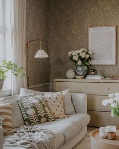 a living room filled with furniture and flowers in vases on the coffee table next to a window