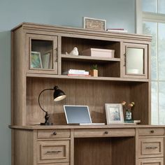 a wooden desk with a laptop on it in front of a bookcase and window