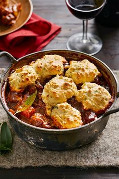 a pot filled with meat and vegetables next to two glasses of wine