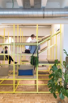 two people sitting on bunk beds in a room with wooden floors and yellow metal frames