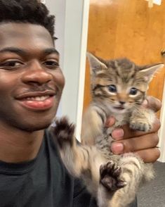 a man holding a small kitten in his right hand and smiling at the camera,