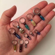 a person's hand holding many different types of glass beads and magnifying glasses