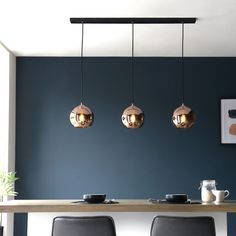 three lights hanging over a table in a room with blue walls and black leather chairs