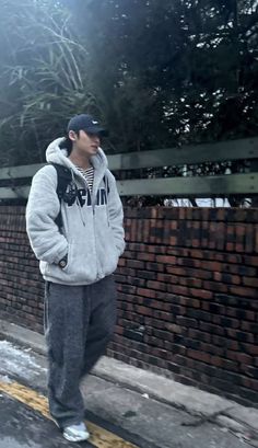 a young man standing on the side of a road next to a brick wall wearing a hoodie