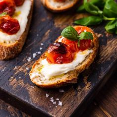 bread topped with cheese and toppings on a wooden cutting board next to basil leaves