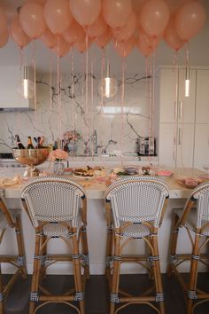 balloons are hanging from the ceiling above a kitchen island with chairs and counter tops in front of it