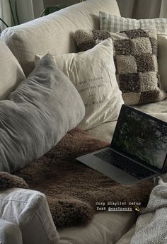 an open laptop computer sitting on top of a couch covered in pillows and throw blankets