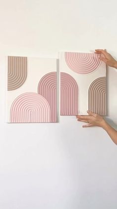 two pink and brown art pieces on a white wall with one being held up against the wall