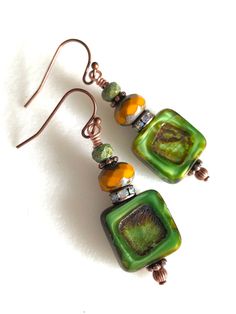 Gorgeous earthy green and mustard  Czech glass earrings featuring 14 mm table cut opaque green Czech squares with rustic Picasso finish. Copper Crystal rondelles, tiny olivine Czech glass beads and copper daisies are add accents.  Beautiful rich green Czech glass beads are wire wrapped on antique copper French hooks. Drop is 1 1/2 inch. Artisan Green Rectangular Jewelry, Green Rectangular Artisan Jewelry, Artisan Rectangular Green Jewelry, Handmade Square Green Jewelry, Czech Glass Bead Earrings, Handmade Square Green Earrings, Handmade Green Square Earrings, Square Green Handmade Earrings, Green Bohemian Rectangular Earrings