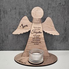 an angel shaped candle holder with the words son written on it and a glass in front