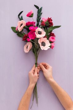 two hands are holding flowers on a purple background