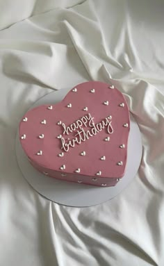 a pink heart shaped cake sitting on top of a white tablecloth covered bedding