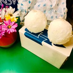 two balls of white cake sitting on top of a box next to flowers and tissues