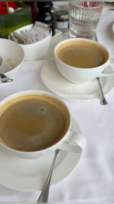 two cups of coffee sitting on top of white saucers and spoons next to each other