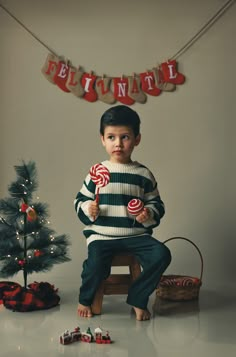 a young boy sitting on a chair holding a lollipop in front of a christmas tree