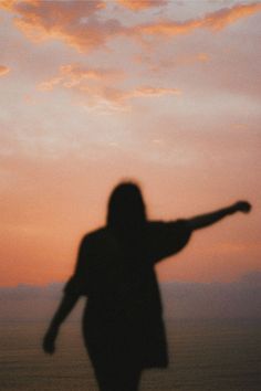 a person standing on the beach with their arms outstretched in front of an orange and pink sky