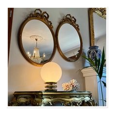 two mirrors are hanging on the wall above a table with a lamp and vases