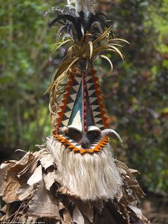 an elaborately decorated mask with feathers on it's head and palm trees in the background