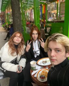 three people sitting at a table with food in front of them and one person holding up the peace sign