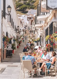 people are sitting at tables in an alleyway with flowers and potted plants on either side