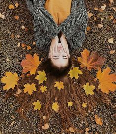 a woman laying on the ground with her hands over her head, surrounded by autumn leaves