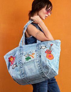 a woman carrying a large denim bag with patches on the front and side, standing against an orange wall