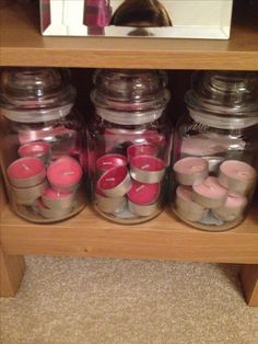 jars filled with candles sitting on top of a wooden shelf next to a cat laying in the background