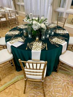 a green table cloth with white flowers and candles on it is surrounded by gold chairs