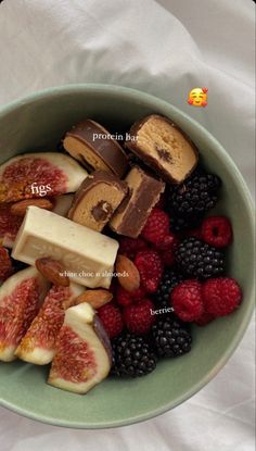 a green bowl filled with assorted fruit and crackers next to raspberries