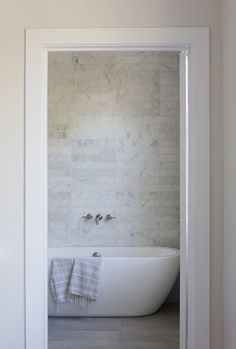 a white bath tub sitting inside of a bathroom next to a doorway with a towel hanging on it