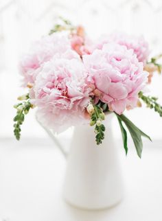 pink carnations in a white vase with greenery on the top and bottom