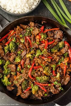 beef and broccoli stir frying in a skillet with rice on the side