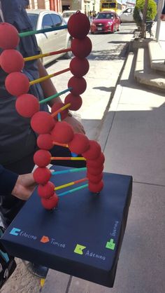 a man sitting on a bench next to a red object with sticks sticking out of it